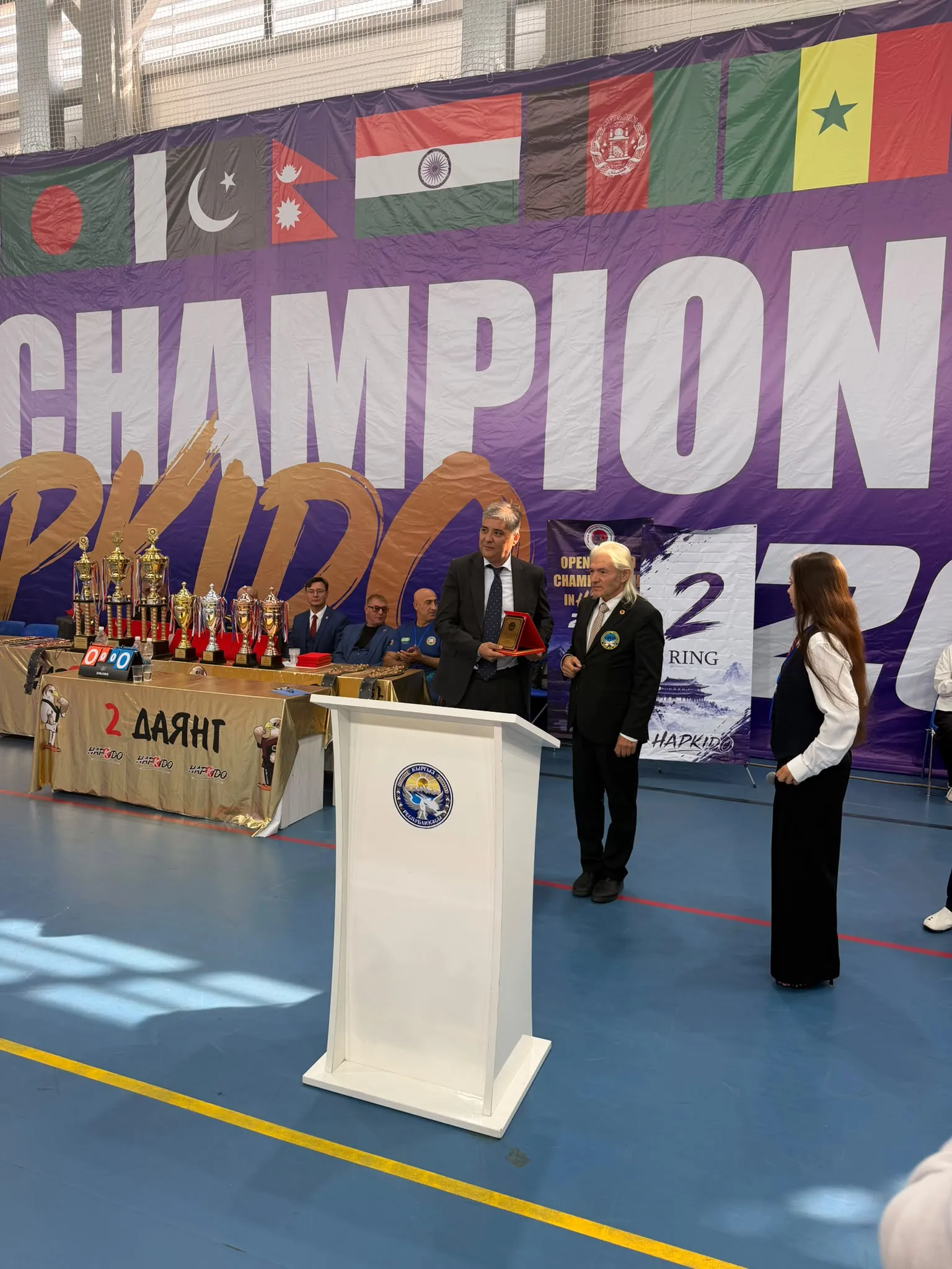 2026 Dünya Hapkido Şampiyonasının açılış konuşmasını yapan Kırgız Cumhuriyeti olimpik olmayan Kültür ve Fiziksel sporlar bakanı Samat Erkinbekov a WAHA Başkanı Şükrü Kınataş Hapkido ya yaptığı katkılardan dolayı bir şilt takdim etti